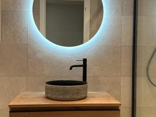 Baño reformado con espejo redondo retroiluminado y lavabo de piedra